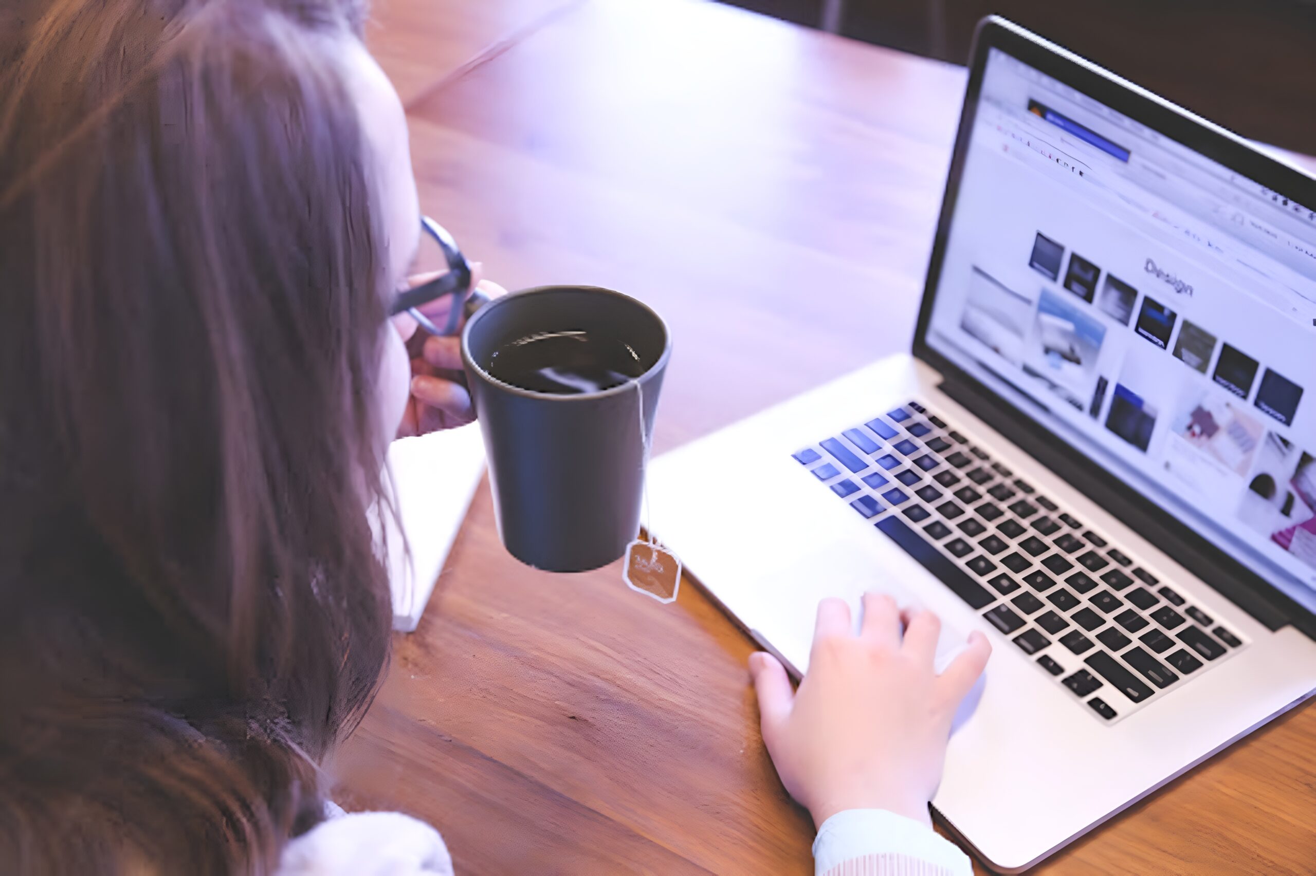  person using a laptop with right hand while holding a tea mug bag-in with left.