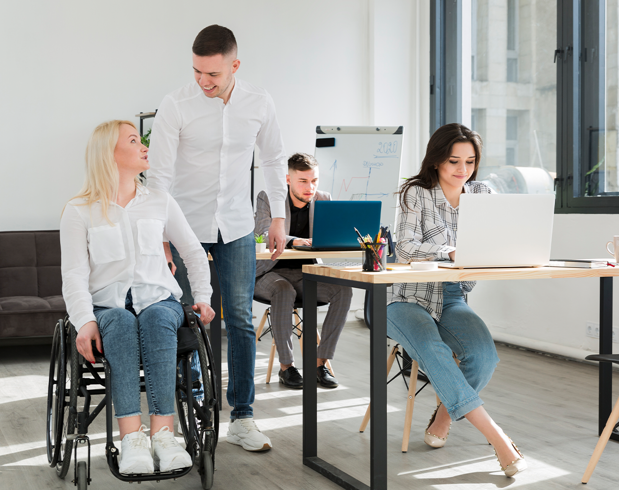 Picture of a man and woman working on laptops, while a man and a woman in a wheel chair walk by.